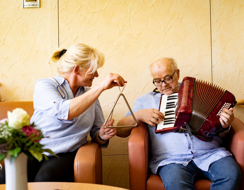 Eine Therapeutin beim Musizieren mit einem Bewohner, der Akkordeon spielt.