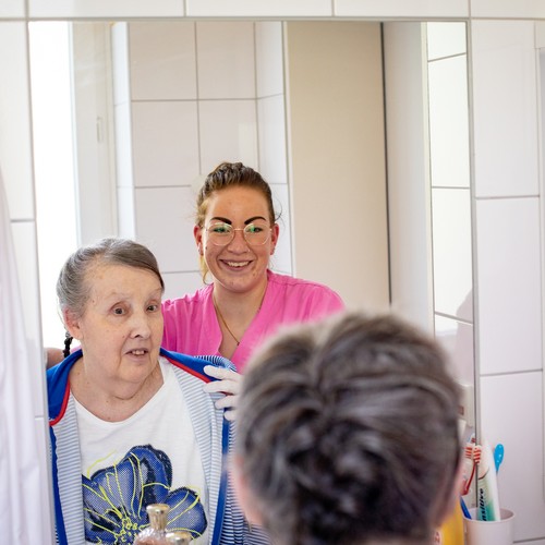 Eine Pflegekraft unterstützt eine Bewohnerin bei der Haarpflege.